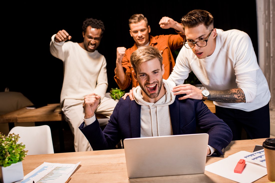 happy multicultural businesspeople showing winner gesture while working at night in office